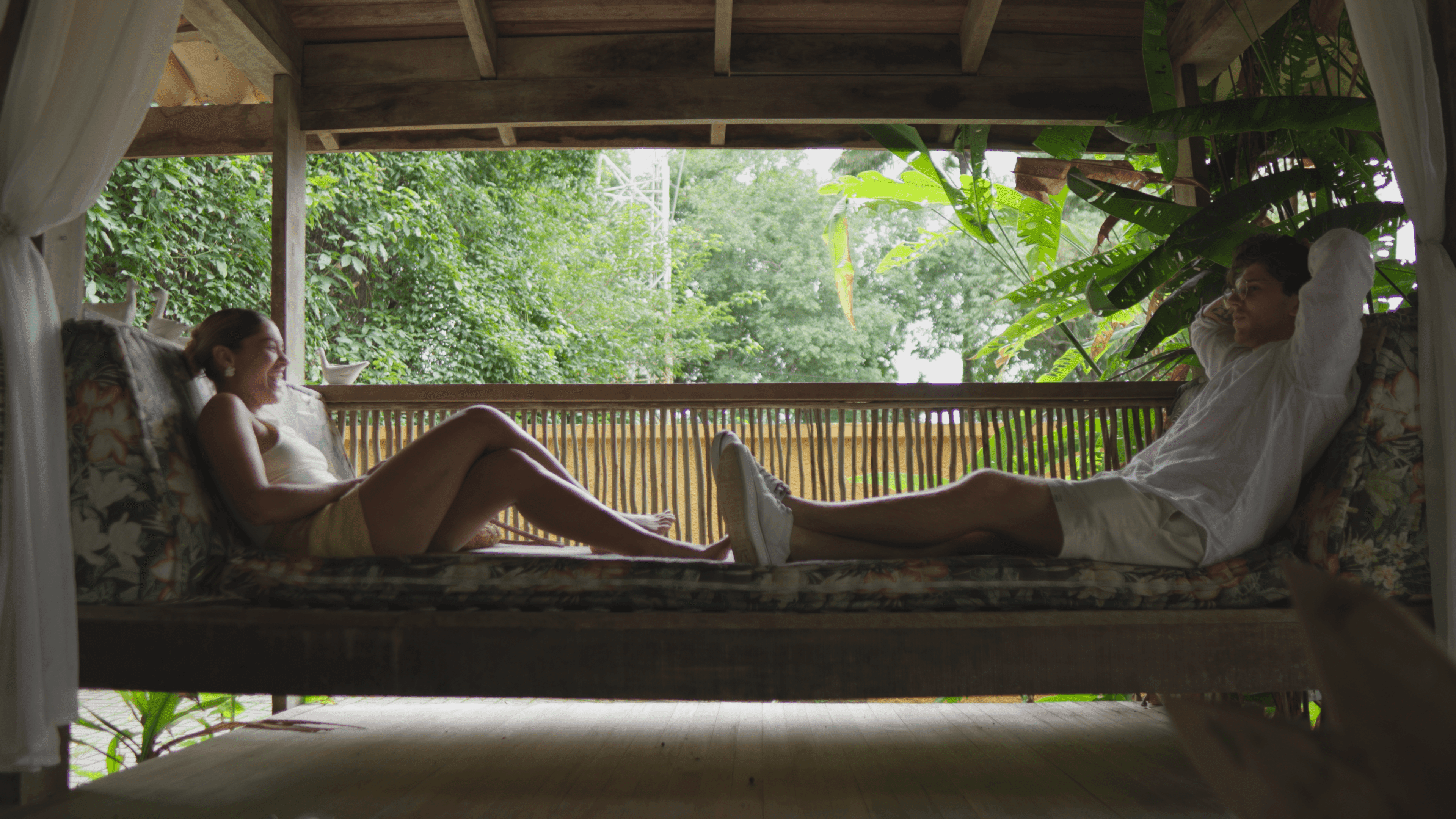 Still from the Alua shoot: a couple resting on a porch swing, facing the forest.