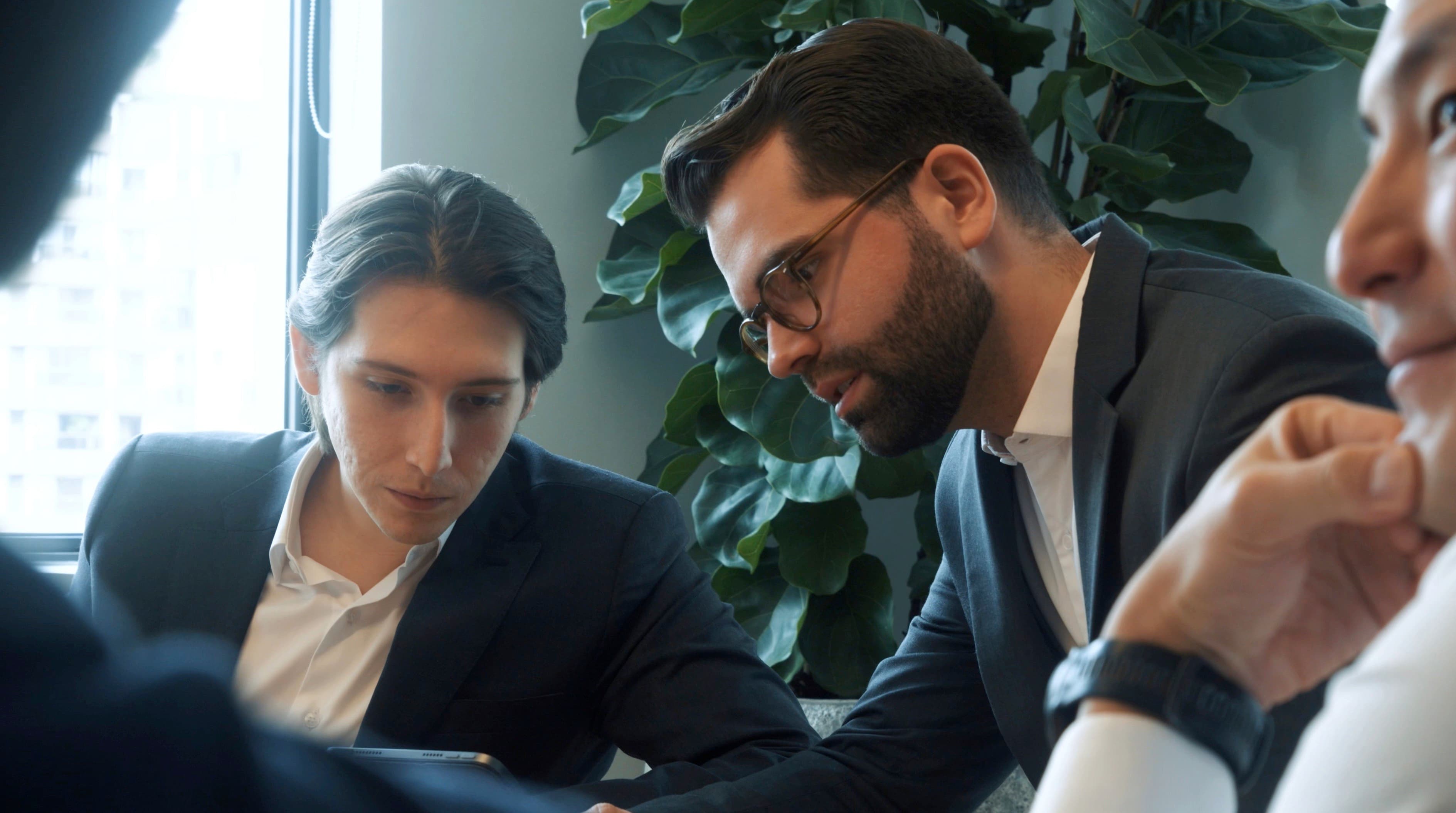 Three people leaning over one screen at a meeting table, reading the same thing.